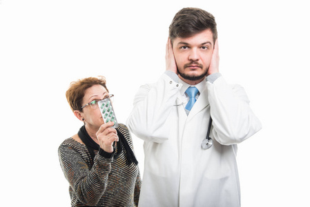 男性医生覆盖的耳朵和女性病人显示药片隔离在白色背景下