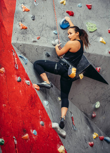 适合运动的学生女孩移动在攀岩墙在健身房