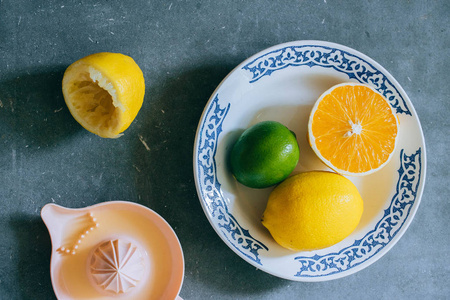 柠檬, 石灰, 橙色在白色陶瓷板材与样式, 一个柑橘榨汁机在灰色具体背景。制作新鲜柠檬水