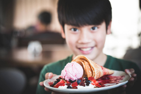 兴奋的亚洲孩子带着微笑的脸显示甜点。把华夫饼放在盘子上