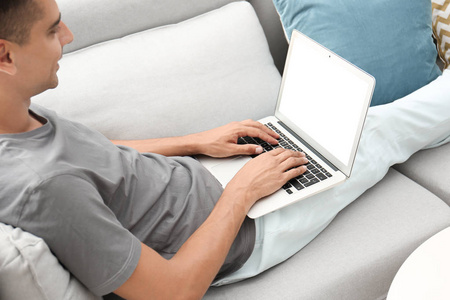 男子在休闲服装使用笔记本电脑在家里的沙发上