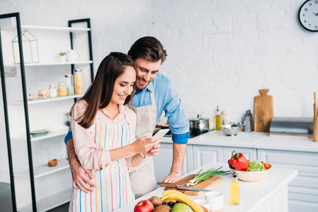 情侣在厨房做饭时拥抱和看智能手机