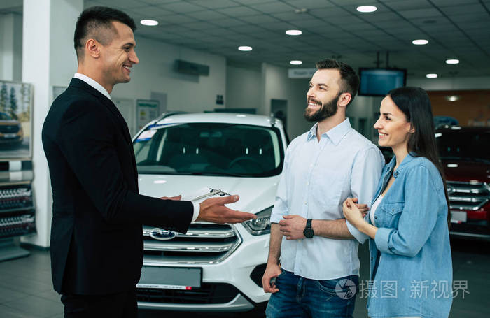 汽车推销员在经销商告诉年轻顾客关于存货在商店.购买汽车概念