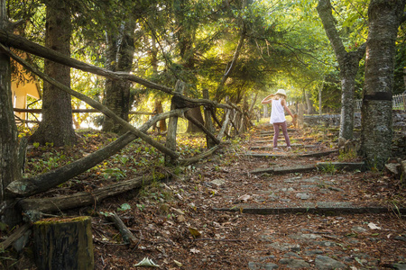 一个戴着帽子的小女孩沿着森林小路奔跑。童话森林中的日落