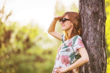 女性戴眼镜和夏天衣服的侧面看森林树干