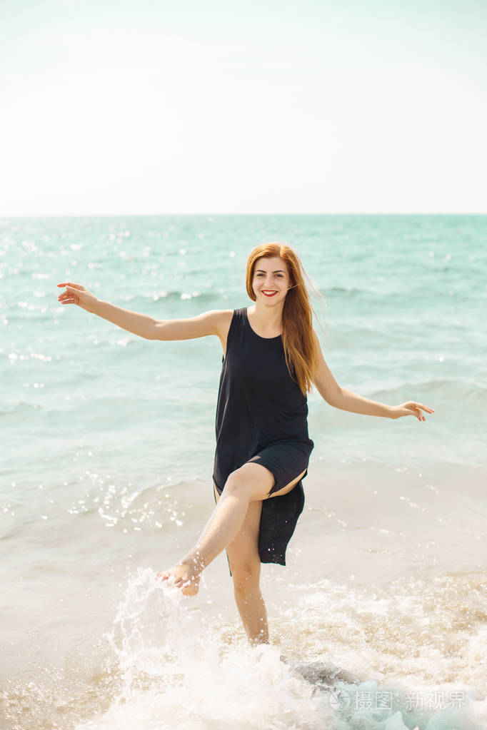 穿着黑色连衣裙的性感红衣女郎赤脚在沙滩上裸泳