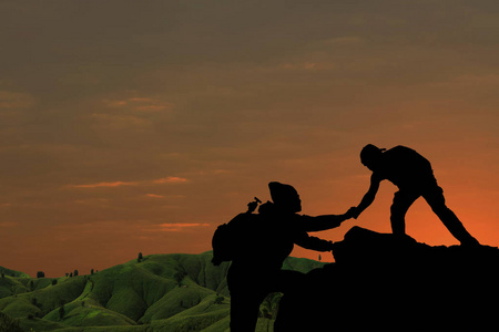 朋友互相帮助设法到达山顶在美妙的夏天日落期间照片