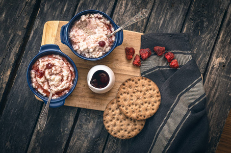 大麦粥与草莓果酱在蓝色陶瓷壶和面包上黑暗的老木背景。健康早餐