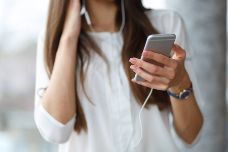 一个漂亮的女孩正在咖啡馆里听着她的智能手机上的音乐.