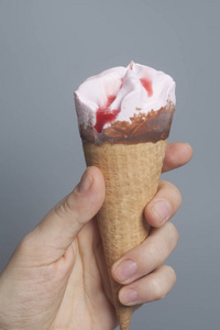 妇女手拿着草莓冰淇淋锥在灰色背景