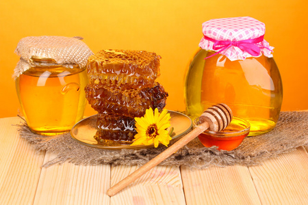蜂蜜和蜂窝橙色背景上的木桌上的 jars