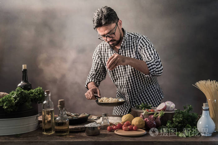 小胡子厨师添加香料和盐在厨房的意大利面条