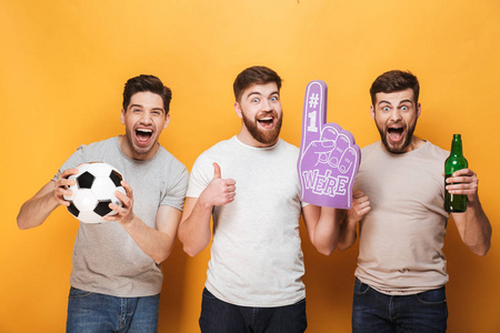 三年轻人激动的球员橄榄球爱好者庆祝孤立在黄色背景照片