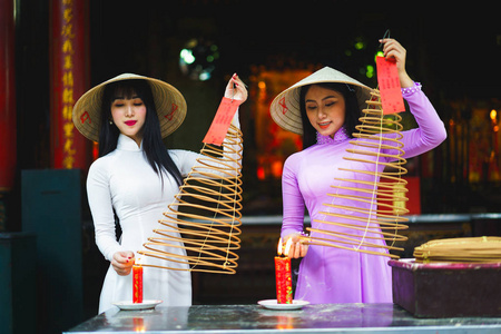 越南妇女穿着传统礼服, 用香棍祈祷在中国寺庙的燃烧锅里, 胡志明越南