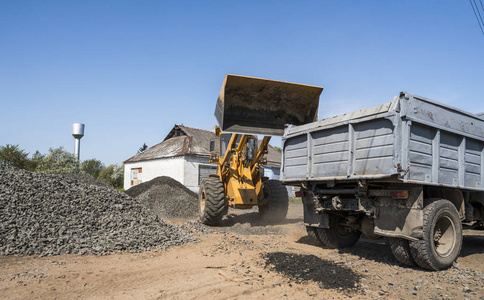 在公路建设工程中, 黄色装载者向卡车运送碎石。道路上的石头。卸石