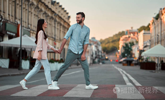 可爱的浪漫情侣在城市散步时一起在人行横道上漫步.