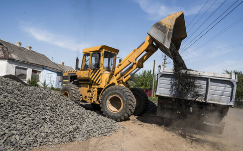 在公路建设工程中, 黄色装载者向卡车运送碎石。道路上的石头。卸石