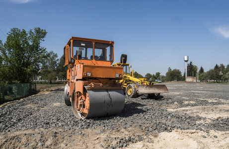 在公路施工中站在石材上的桔光振动压路机及修复有蓝天的沥青路面工程