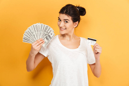照片的开朗年轻漂亮的妇女站在黄色背景下持有货币和信用卡