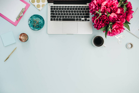 工作区与膝上型电脑和粉红色的牡丹花花束在蓝色背景。平躺, 顶部查看家庭办公办公桌