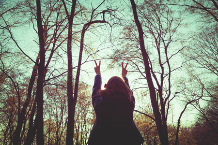 妇女站立的剪影与举手和显示和平标志在森林里