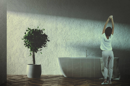 女人靠近一个白色的浴缸, 上面挂着毛巾, 站在简约浴室的木地板上。一棵树在罐子里。3d 渲染模拟色调图像双曝光
