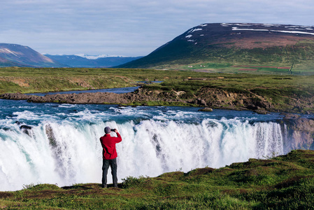 Godafoss 瀑布。美丽的风景在冰岛。穿红夹克的家伙在河边拍照