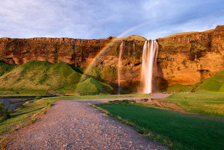 Seljalandsfoss 瀑布。与级联和一条河的夏季景观。令人惊异的光的傍晚的太阳。著名的旅游胜地的冰岛