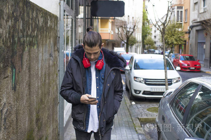 青年用耳机走在街上用手机
