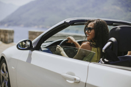 大雪天的车戴墨镜的年轻女子驾驶着她的敞篷车, 在晴朗的阳光明媚的天