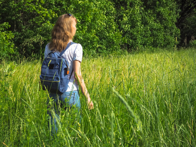 一个身材苗条的女人带着背包在高高的草地上旅行。