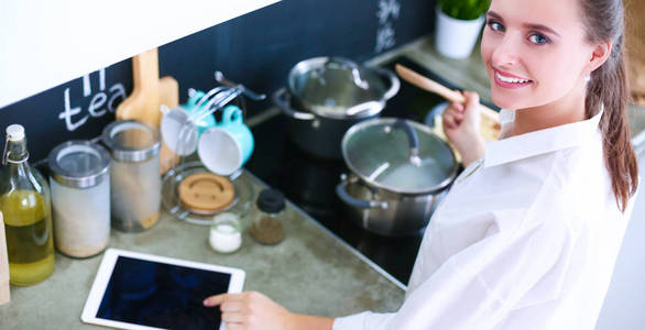 年轻女子在家里的厨房里使用平板电脑和喝咖啡