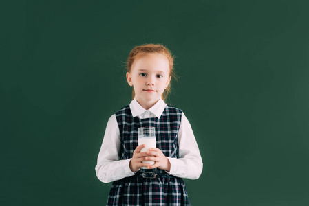 可爱的小女生抱着玻璃牛奶, 微笑着站在黑板旁边的相机