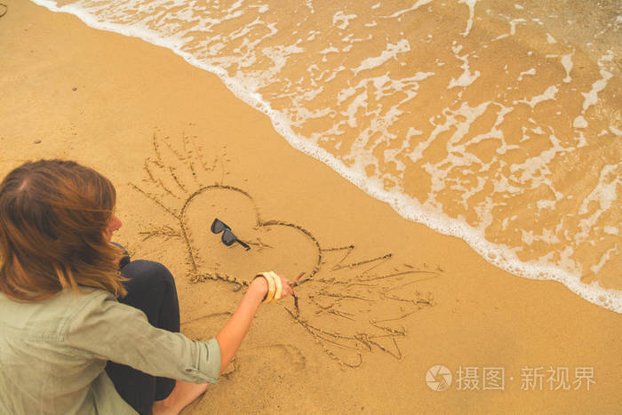 在海洋沙滩上画一颗心的女孩