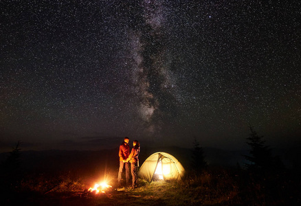 在燃烧的篝火旁, 照明的旅游帐篷, 山地自行车在惊人的美丽的夜空