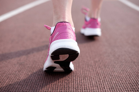 运动。女性腿在粉红色运动鞋在奔跑轨道体育场。一个跑步女工的运动鞋特写。概念运行