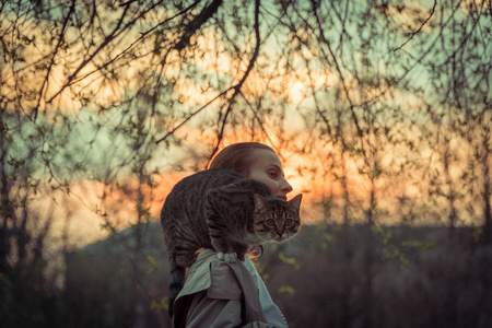 猫在皮带上。一个女孩正带着一只坐在她肩上的猫散步。