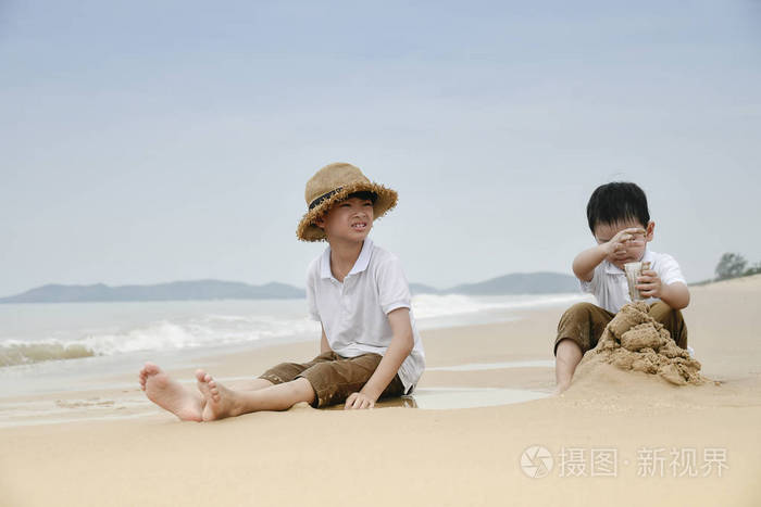 快乐亚洲男孩建筑沙子城堡在海滩