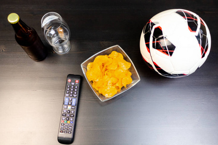 人们准备用啤酒在电视上观看足球比赛。桌子上有啤酒, 球, 电视遥控器, 小吃。工艺啤酒。光背景。从顶部的视图