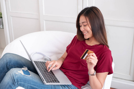 关闭妇女持有信用卡和使用笔记本电脑网上购物在沙发上的房子. 数字支付营销技术理念