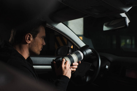 集中的男性做监视由照相机与透镜从他的汽车