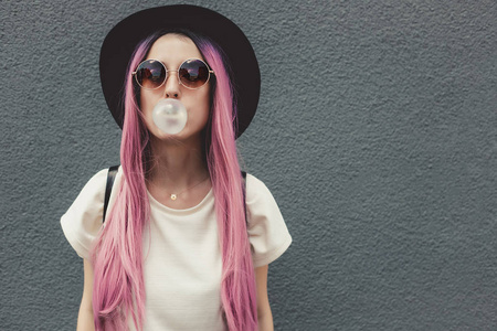 时尚的年轻时髦的女人与长粉红色的头发吹气泡泡沫口香糖
