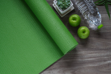 绿色瑜伽垫在一个木质的背景与绿色的苹果和瓶装水。积极健康的生活方式背景概念