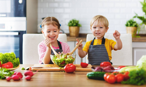 健康的饮食。快乐的孩子们准备和在厨房吃蔬菜沙拉