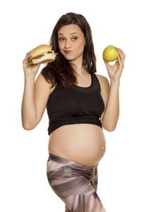 饥饿的孕妇选择在一个苹果和一个汉堡包的白色背景