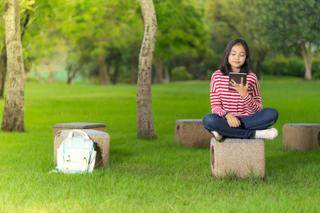 在阳光明媚的夏日, 在学校公园使用数码平板电脑的亚洲学生女孩