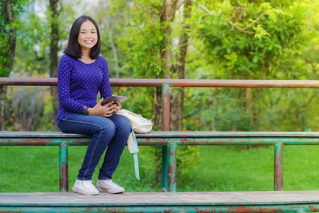 在阳光明媚的夏日, 在公园里使用数码平板电脑的亚洲学生女孩