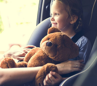 母亲帮忙把安全带给小女儿, 小女孩与泰迪熊在儿童安全座椅上的位置