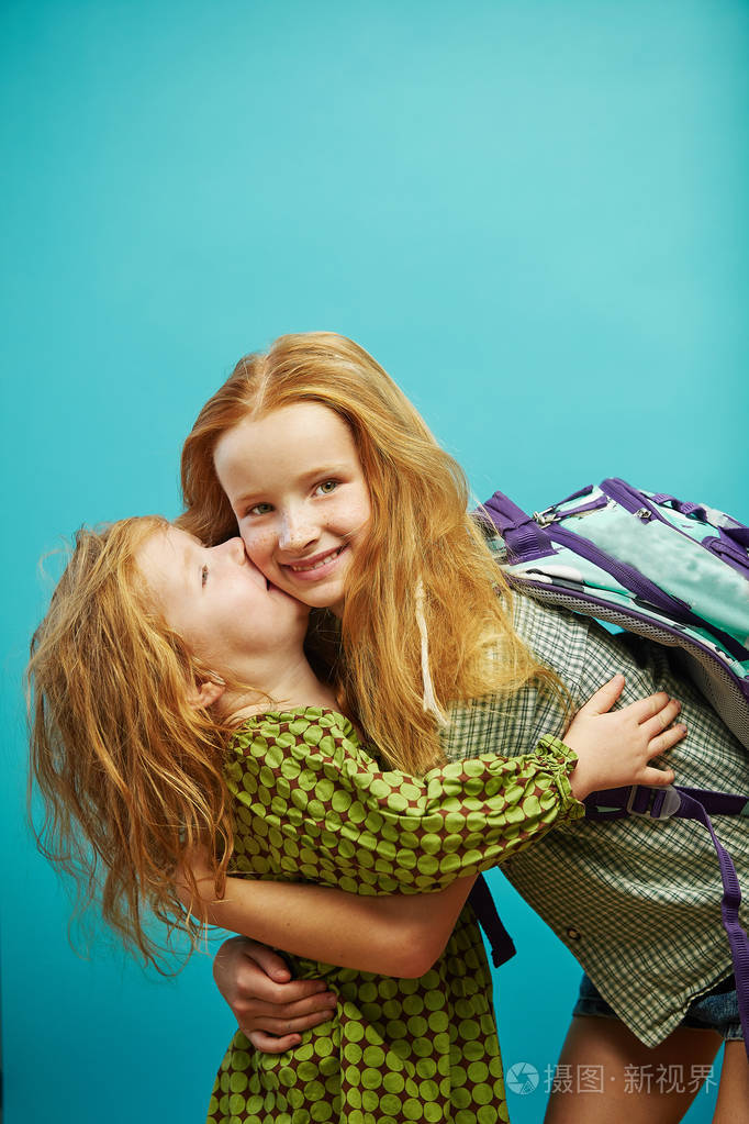 小女孩亲吻她的老姐姐在蓝色背景