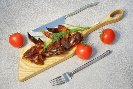美味的烟熏鸡翅在切割板上作为一个盘子, 用莳萝, 葱和西红柿, 配叉和刀, 顶部视图, 对角线组成
